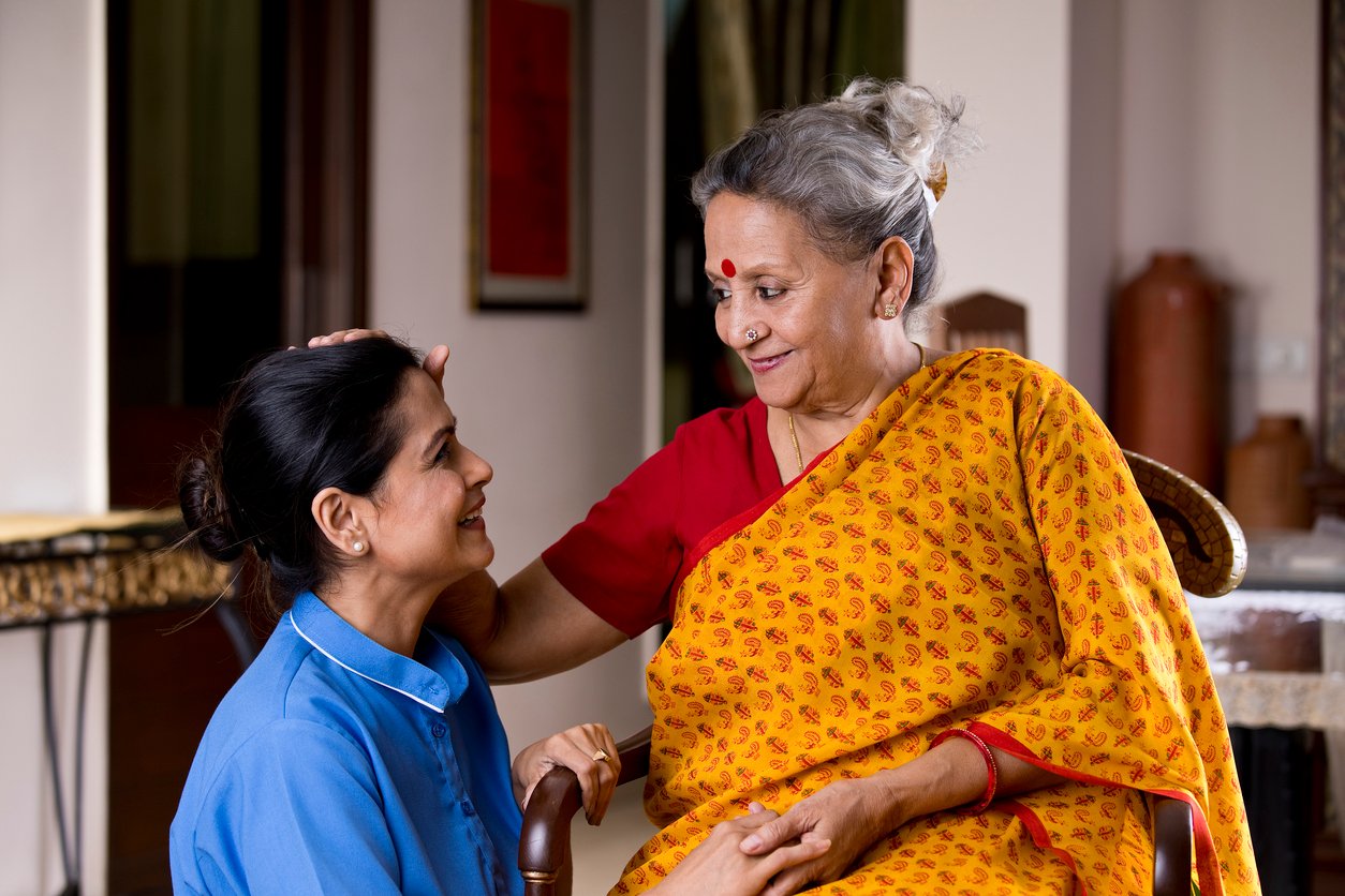 Happy old woman giving blessings to female nurse at home